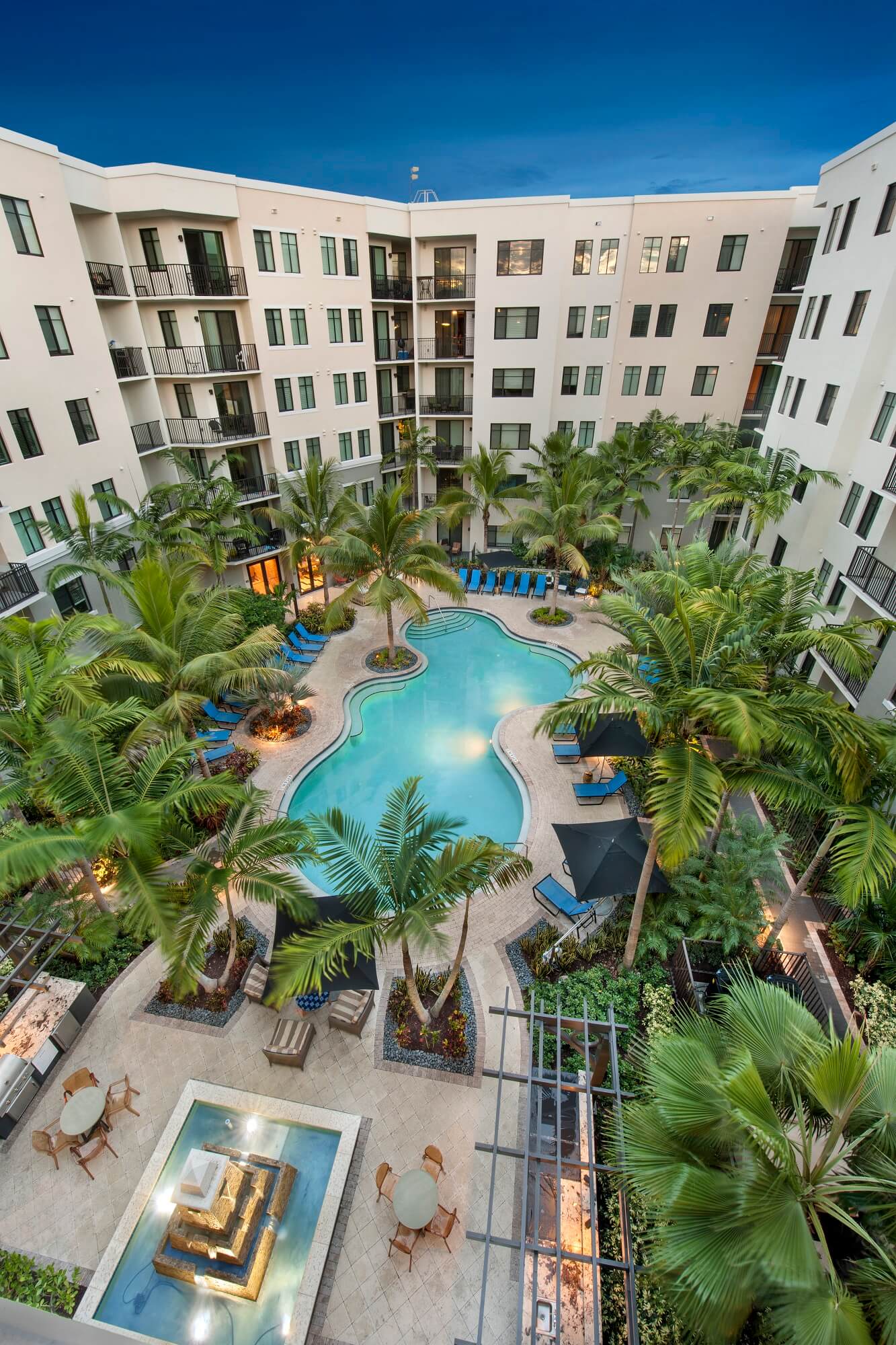Aerial view of Advenir at Lighthouse Point luxury apartment courtyard with palm trees and pool under a clear blue sky.